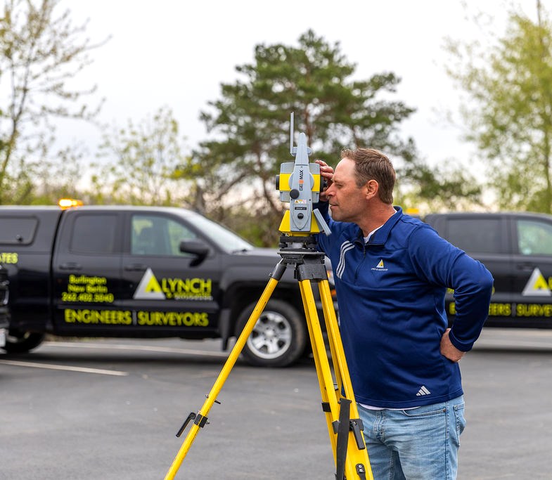 Lynch surveyor operating a robotic total station beside a company survey truck